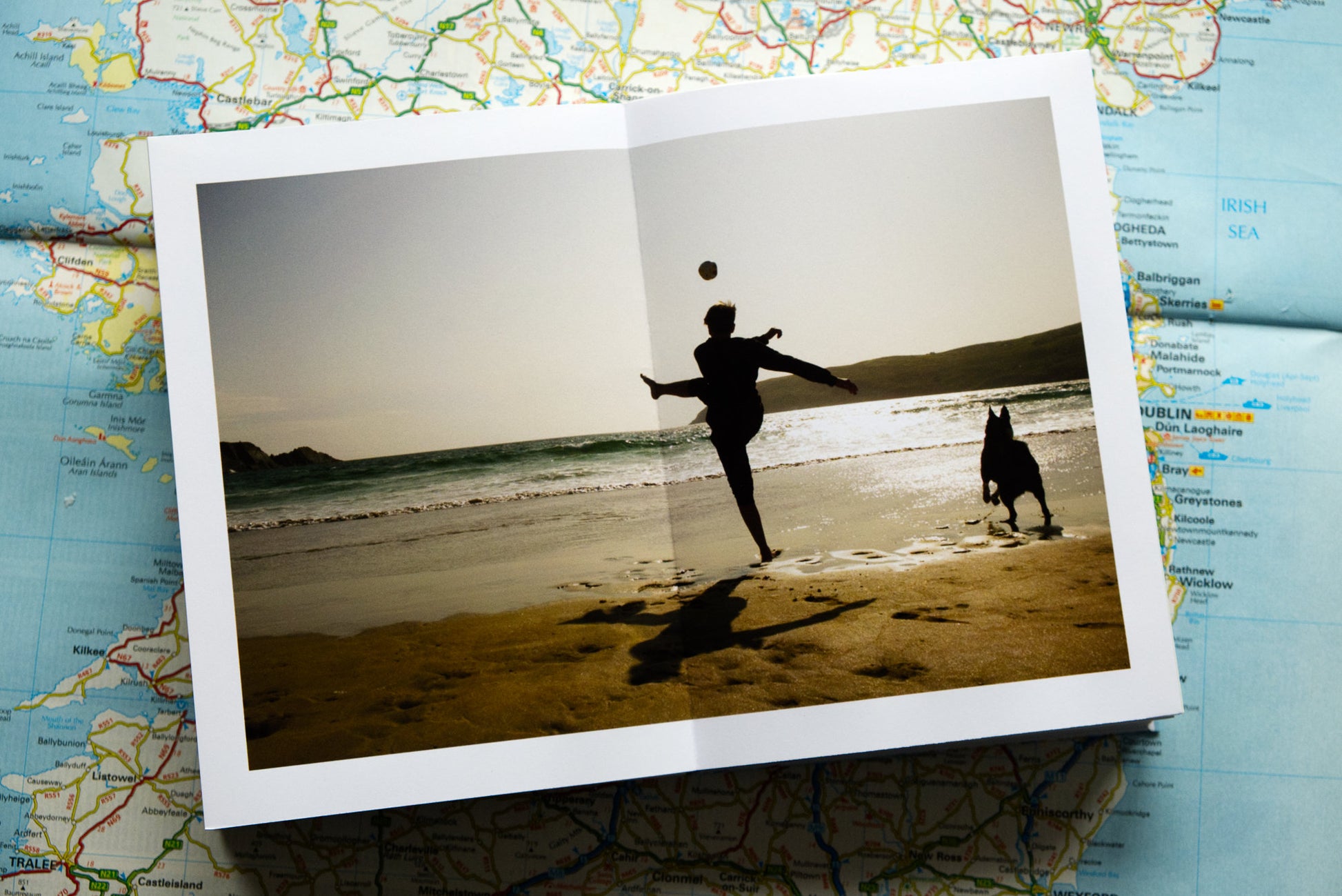 product photograph of handmade photography book showing interior spread of photograph of boy kicking ball into the sea with his dog close by